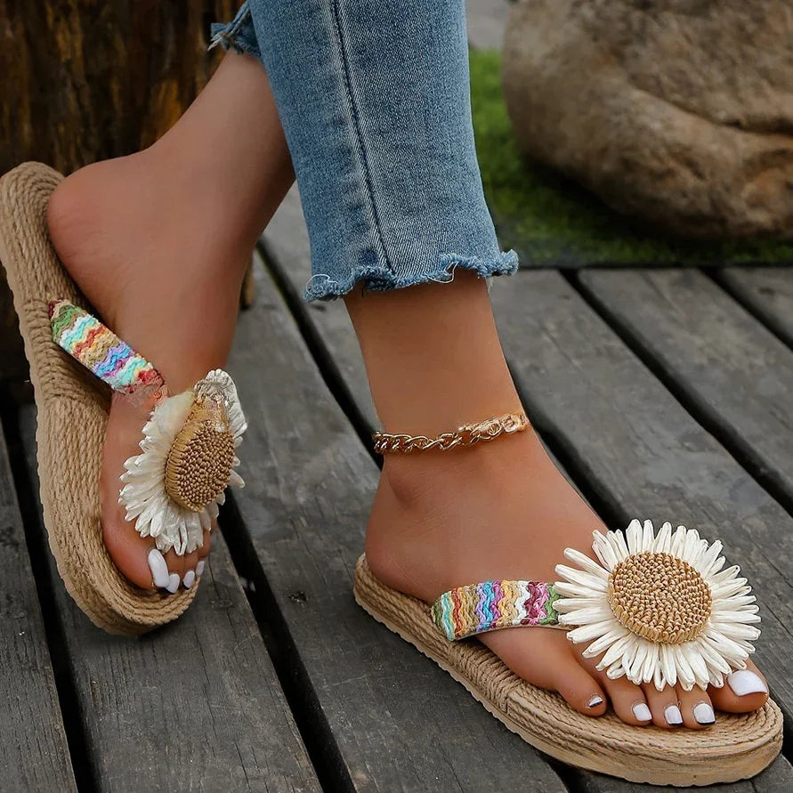 Feet wearing woven sandals with large daisy flower detail and rainbow straps on wooden deck