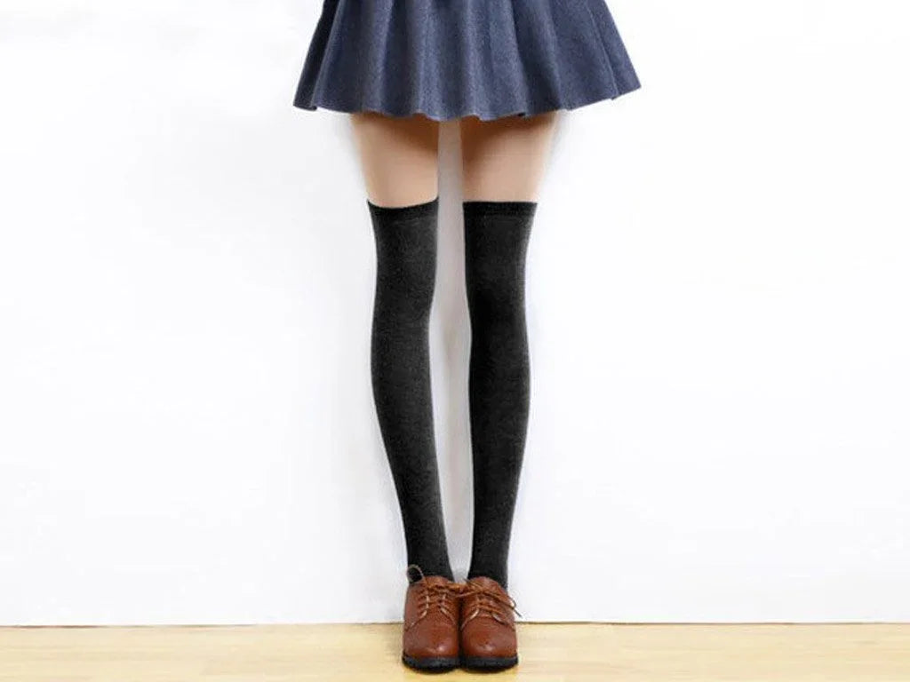 Woman wearing black knee-high socks with brown shoes and a blue skirt against white background