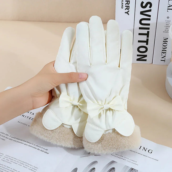 Hand holding elegant white winter gloves with bows and soft beige fur cuffs on table