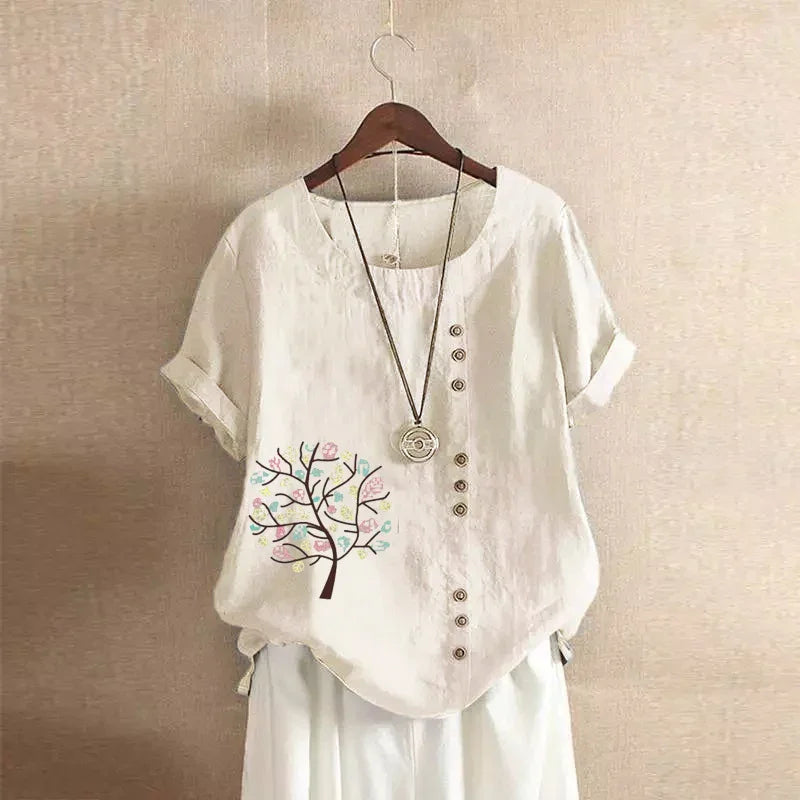Beige linen short-sleeve blouse with buttons and a colorful tree print, paired with white pants