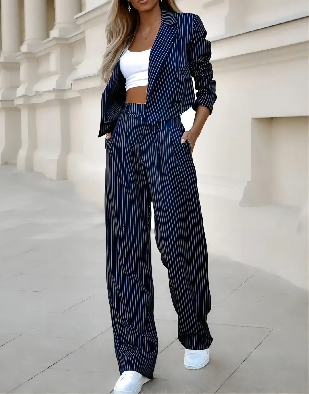Woman wearing navy blue pinstripe suit with wide-leg trousers and cropped blazer over white crop top and sneakers