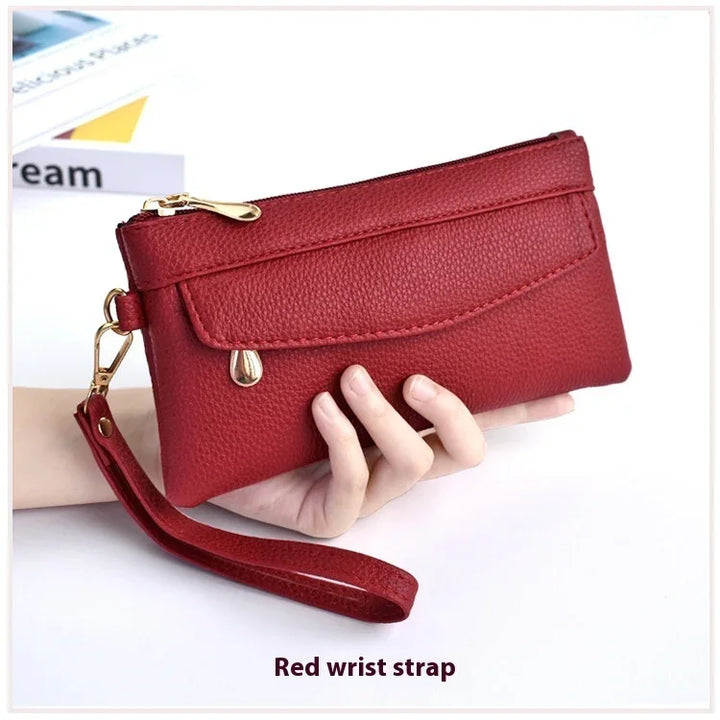 Hand holding red textured leather wristlet wallet with gold zipper and wrist strap
