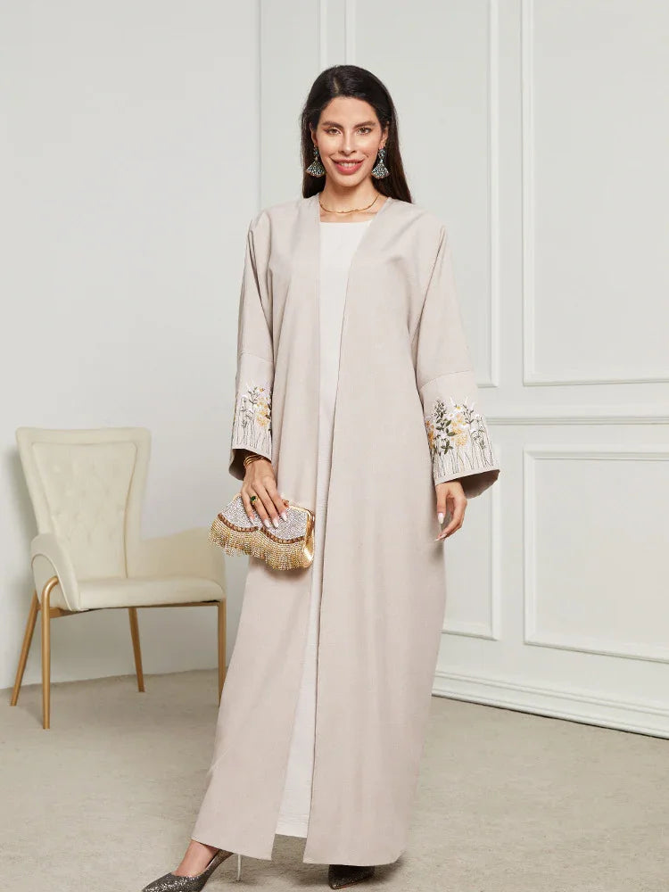 Smiling woman in beige abaya with floral sleeve embroidery holding beaded clutch in elegant room
