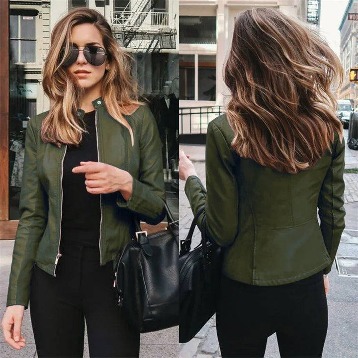 Woman wearing stylish olive green leather jacket and black pants, posing outdoors with sunglasses and black handbag
