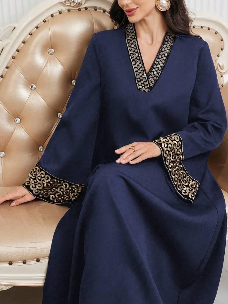 Woman wearing a navy blue abaya with gold embroidered cuffs and neckline sitting on a beige tufted sofa