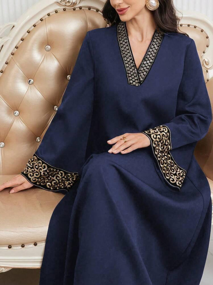 Woman wearing a navy blue abaya with gold embroidered cuffs and neckline sitting on a beige tufted sofa