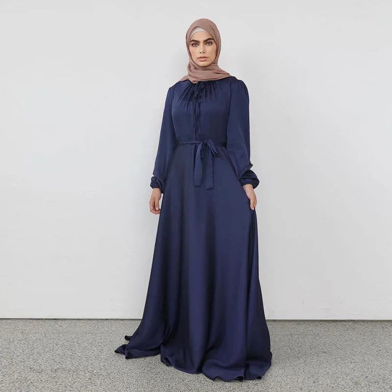 Woman wearing navy blue long-sleeve modest maxi dress with belt and beige hijab on gray floor