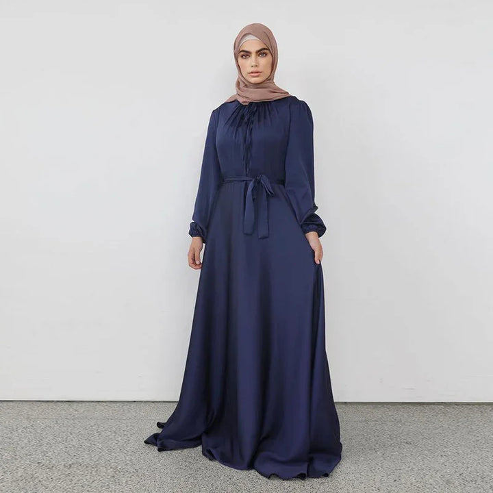 Woman wearing navy blue long-sleeve modest maxi dress with belt and beige hijab on gray floor