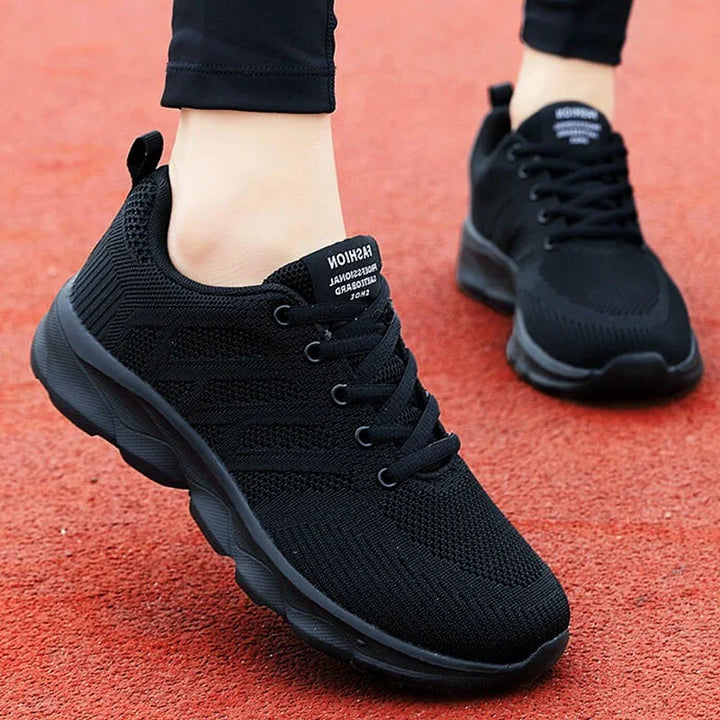 Close-up of black athletic sneakers with mesh fabric and laces on red running track