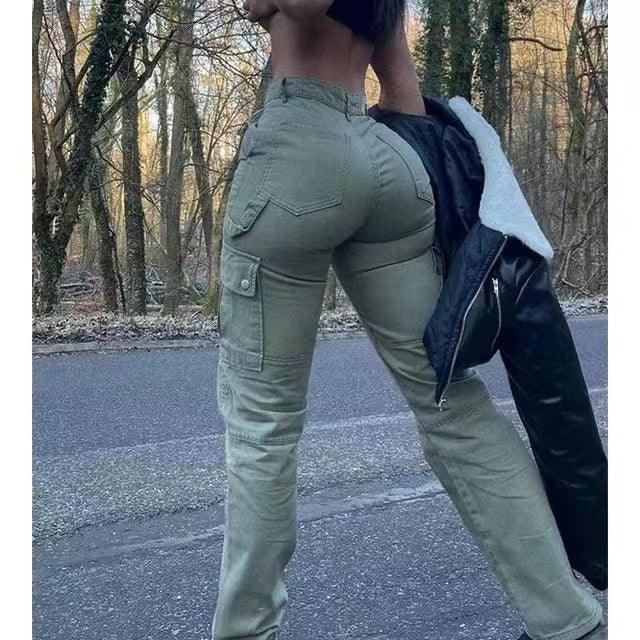 Woman wearing khaki cargo pants standing on forest road holding black jacket, bare midriff visible