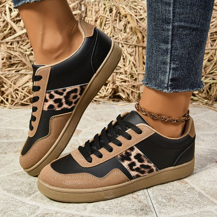 Black and brown casual sneakers with leopard print details worn with dark blue jeans and ankle bracelet on tiled floor