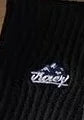 Close-up of black knit fabric with white embroidered text logo reading 'Vacay'