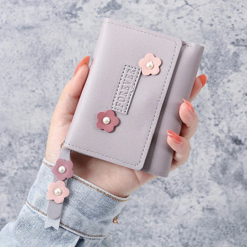 Hand holding lavender wallet with pink flower appliques and pearl accents on textured grey background