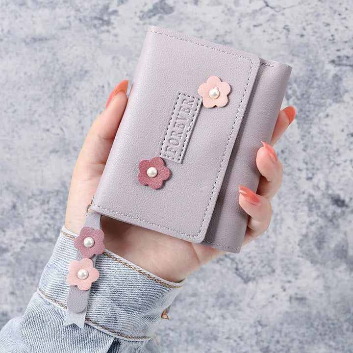 Hand holding lavender wallet with pink flower appliques and pearl accents on textured grey background