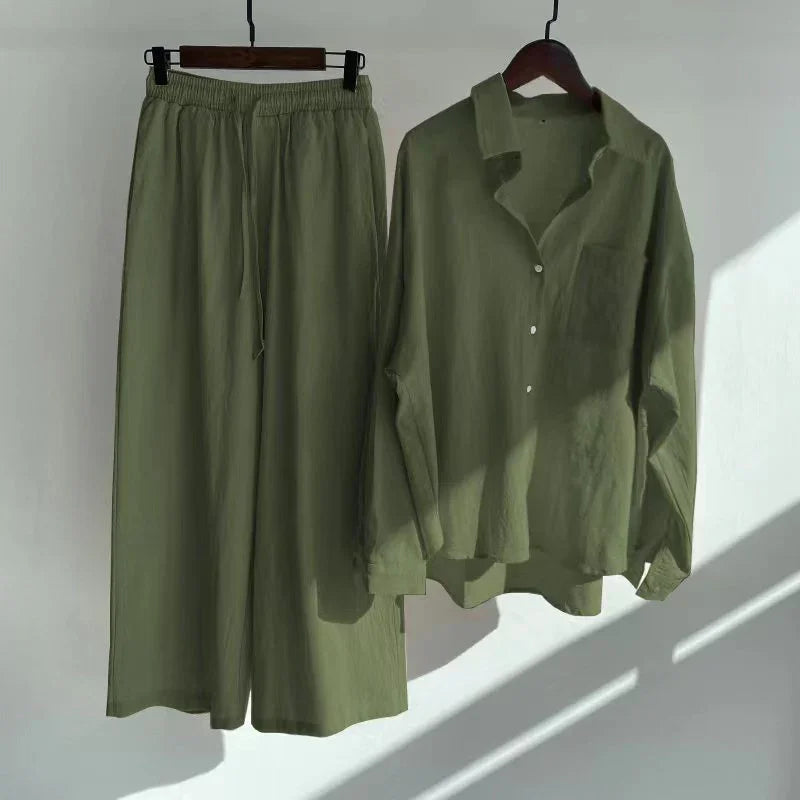 Olive green casual linen shirt and wide-leg pants set hanging on wooden hangers against white wall