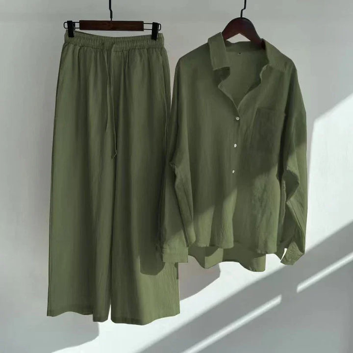 Olive green casual linen shirt and wide-leg pants set hanging on wooden hangers against white wall
