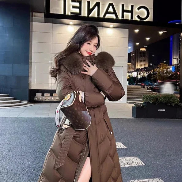 woman in long brown puffer coat with fur collar carrying designer handbag at night by CHANEL storefront