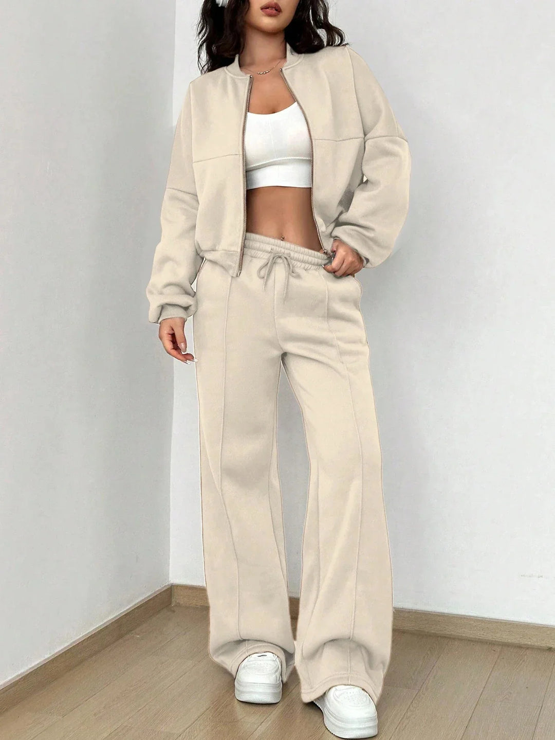 Woman wearing beige zip-up jacket and matching wide-leg pants with white crop top and sneakers