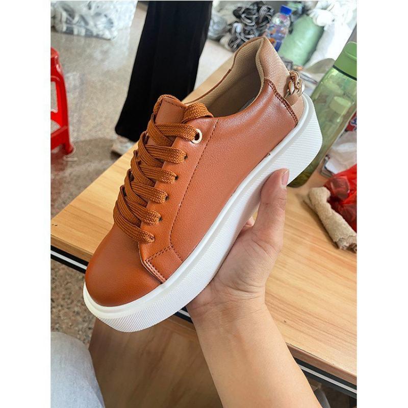Hand holding a casual brown leather sneaker with white sole and matching brown laces indoors