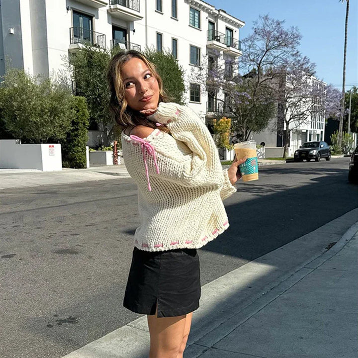 Young woman in chunky white knit sweater with pink accents and black skirt holding iced coffee on city street