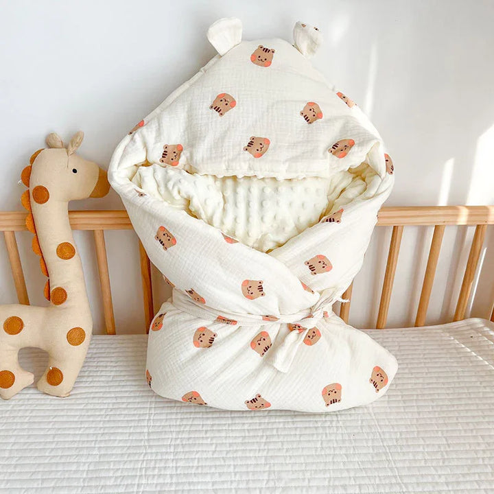 White baby swaddle blanket with animal face prints and ears, soft plush interior, on crib mattress with giraffe plush toy