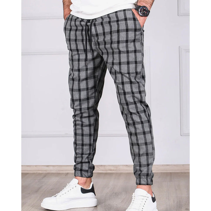 Men's gray and black checkered jogger pants paired with white sneakers on wooden floor