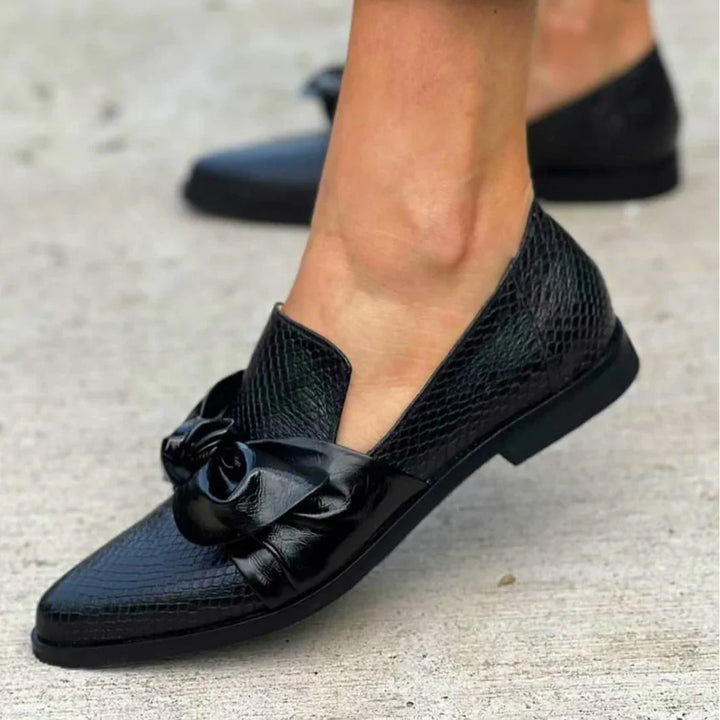 Black textured leather loafers with a decorative knot detail worn on feet outdoors