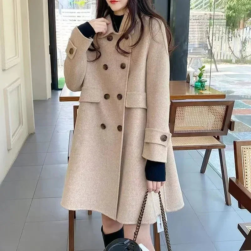 Woman wearing beige double-breasted wool coat indoors holding chain strap bag