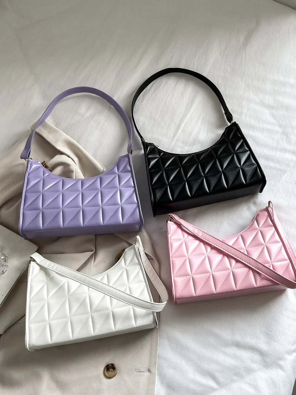 Four quilted leather shoulder bags in purple, black, white, and pink on fabric background