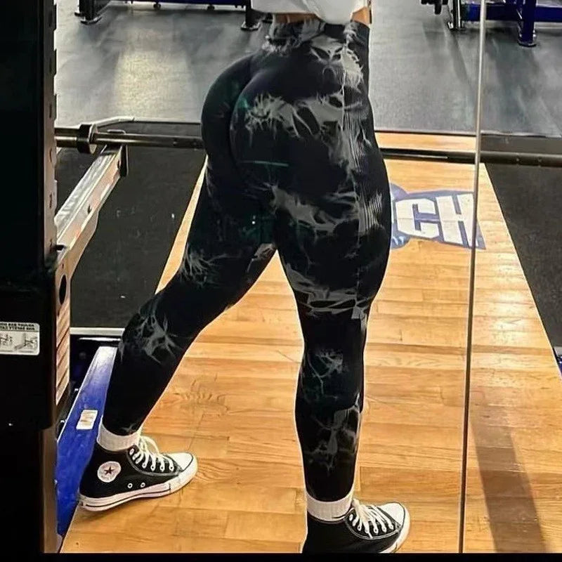 Person wearing black and white patterned leggings and black Converse shoes in a gym squat rack area