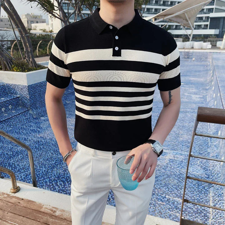 Man wearing black and white striped polo shirt with white pants holding a blue textured glass beside pool