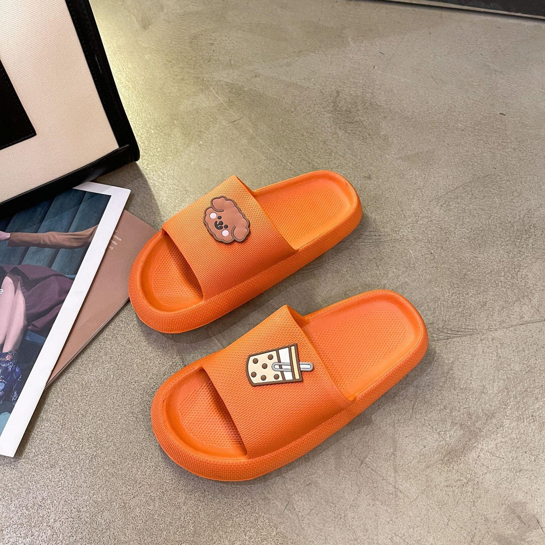 Orange slide sandals with cartoon dog and bubble tea designs on a concrete floor next to magazines