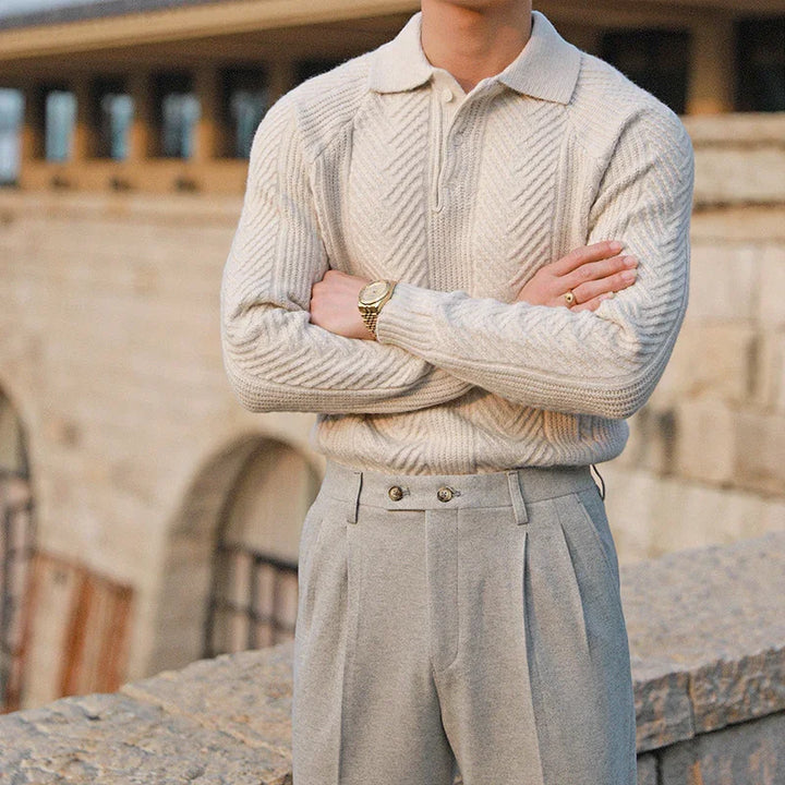 Man wearing a cream knit sweater with zipper collar and gray pleated trousers outdoors