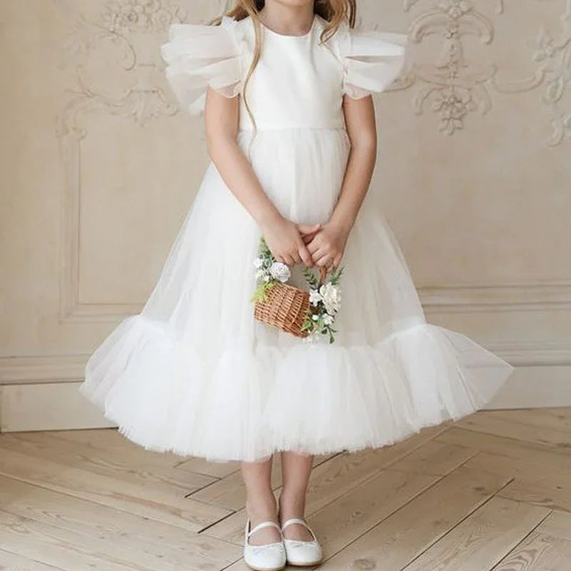 Little girl in white tulle dress with puff sleeves holding a flower basket on wooden floor