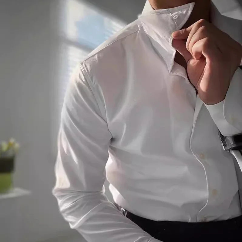 Man adjusting collar of crisp white dress shirt in bright room with soft natural light