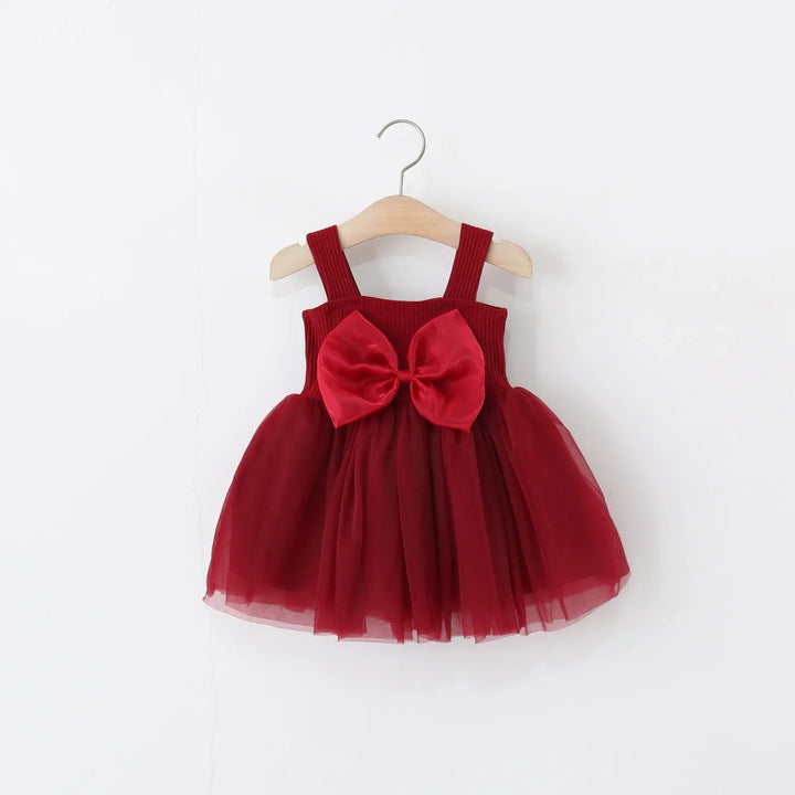 Red toddler dress with tulle skirt and large satin bow hanging on wooden hanger