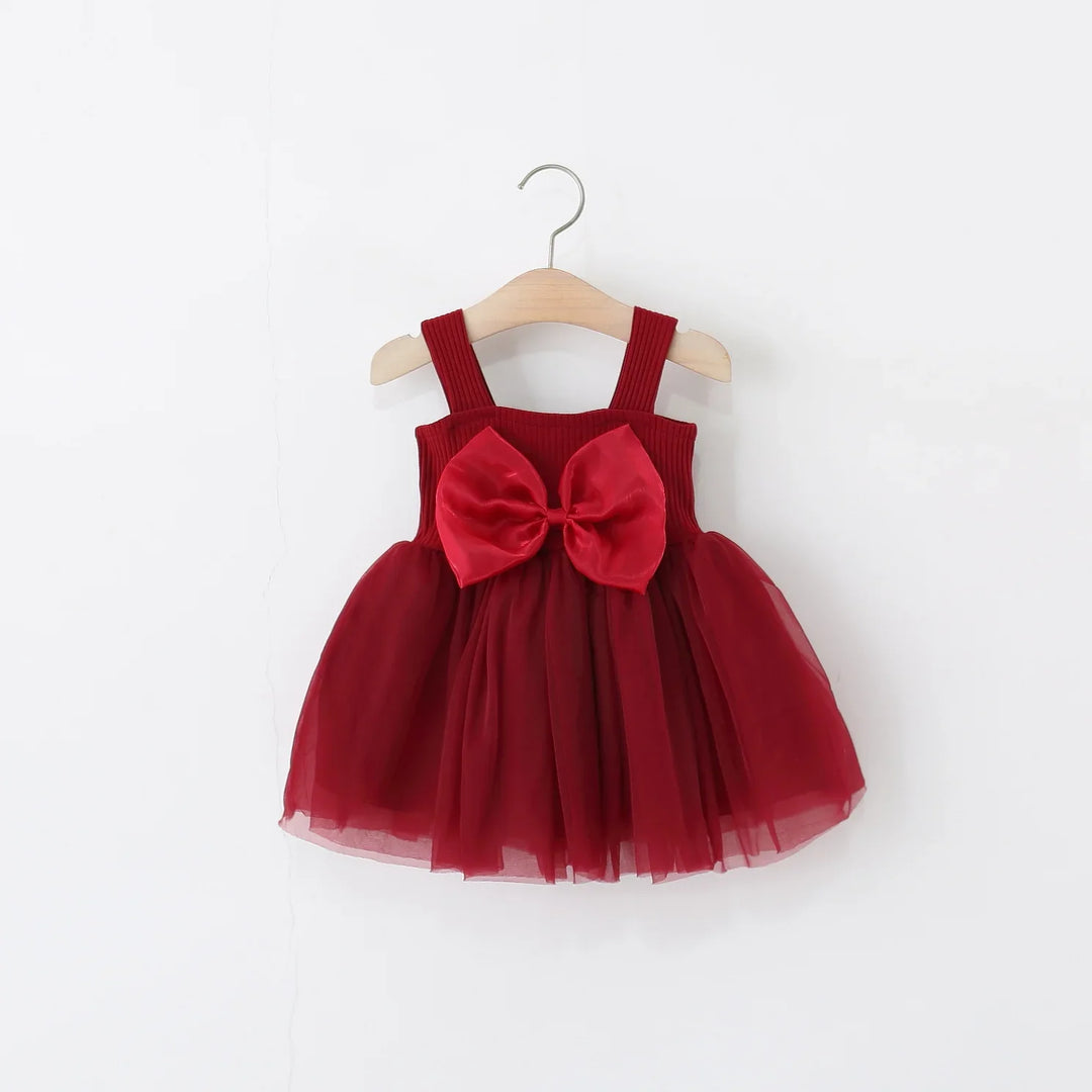 Red toddler dress with wide straps and large bow on tulle skirt, hanging on wooden hanger