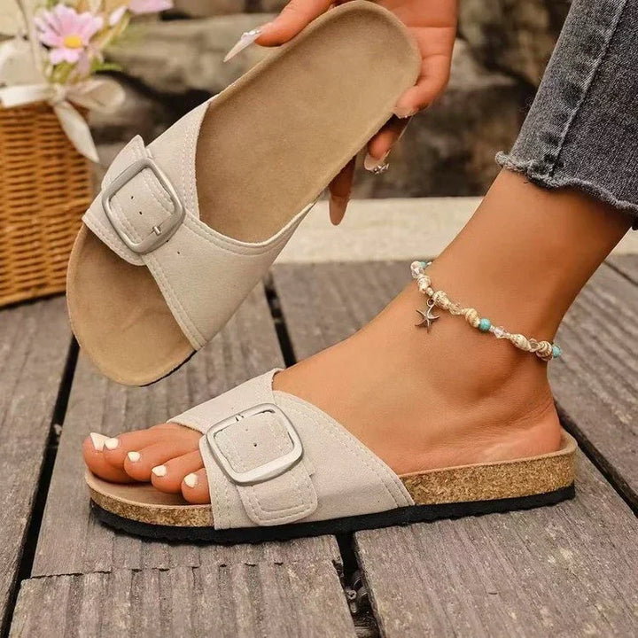 beige slide sandals with buckle detail worn on foot with starfish anklet on wooden floor