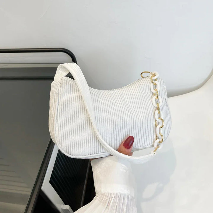 White ribbed handbag with gold and white chain detail held by hand with red nail polish