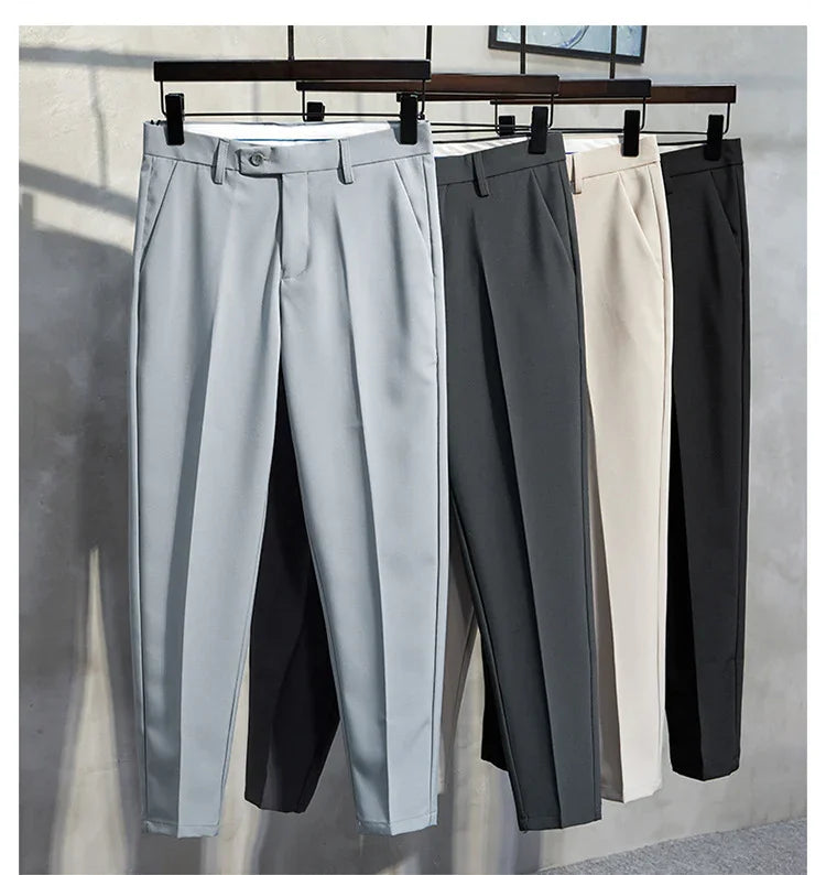 Four pairs of men's formal trousers in light gray, dark gray, beige, and black hanging on wooden hangers
