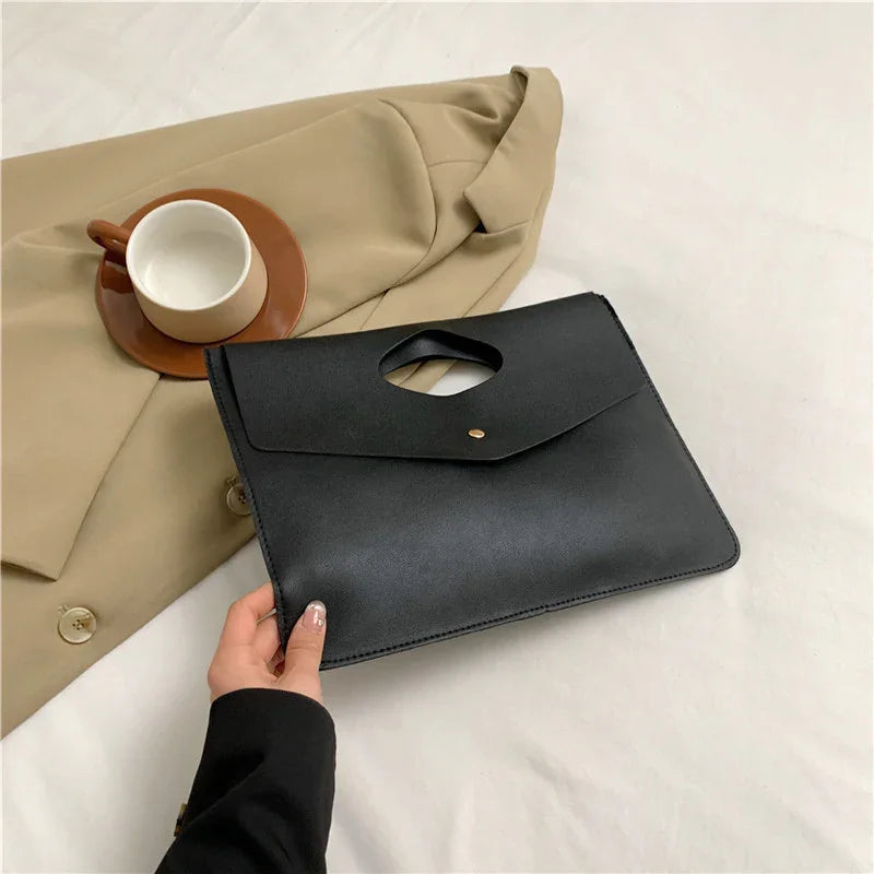 Black leather clutch bag held by hand on beige blazer with empty brown cup and saucer