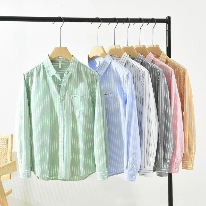 Striped long sleeve shirts in green, blue, white, gray, pink, and mustard hanging on wooden hangers
