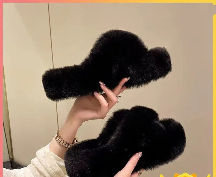 Hands holding black fluffy slippers with soft faux fur against beige background