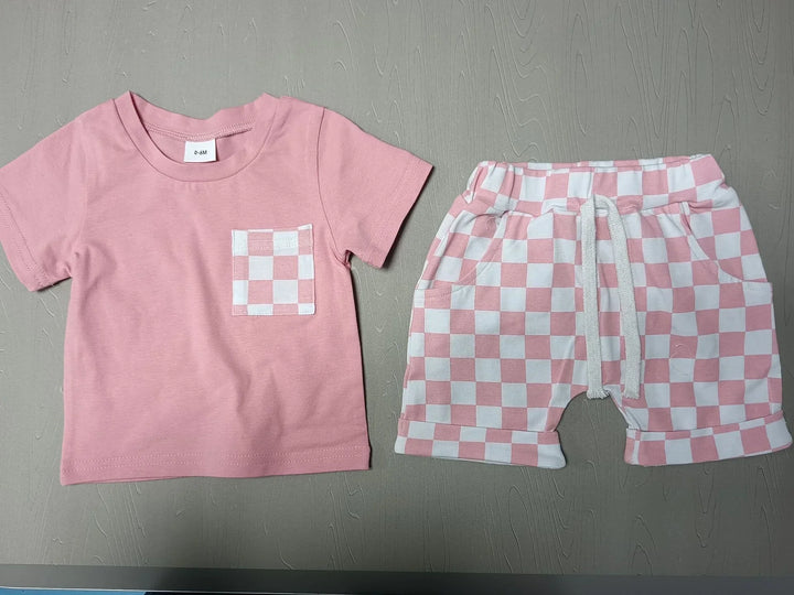 Pink baby outfit with solid shirt and checkered shorts on gray textured background