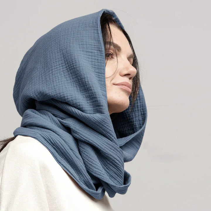 Side view of woman wearing a textured blue hooded scarf with neutral background