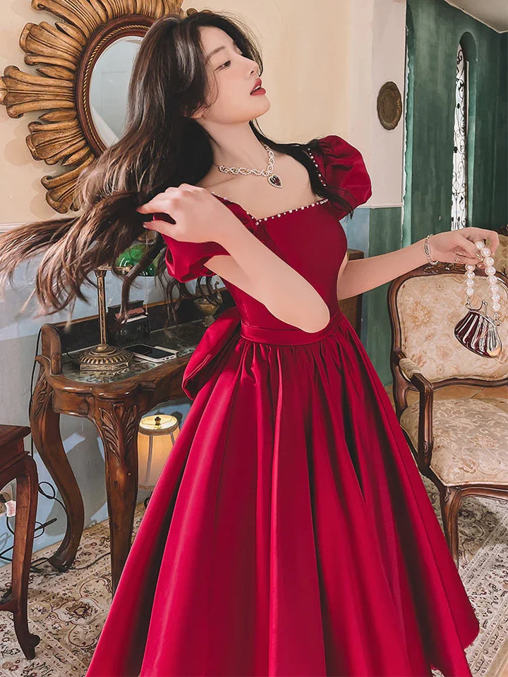 Woman in elegant red puff sleeve dress holding pearl handle purse in vintage-style room