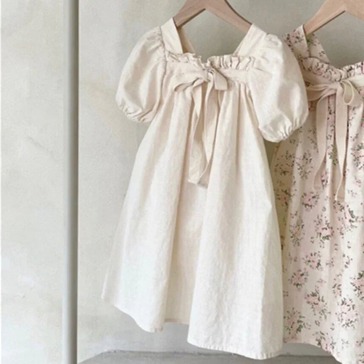 Two toddler dresses on wooden hangers, one cream puff sleeve dress and one floral print dress