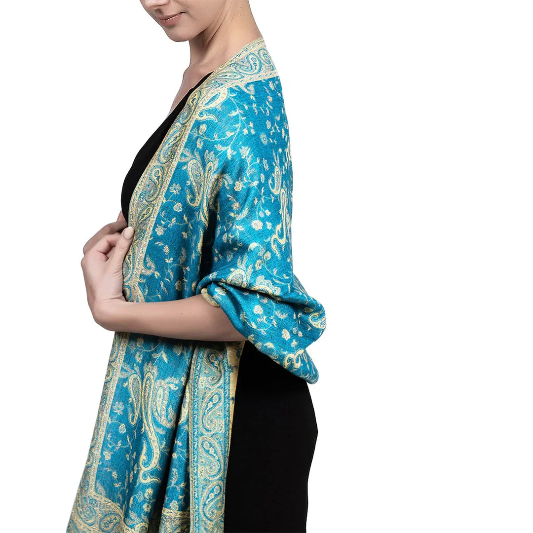 Woman wearing a teal blue paisley patterned shawl over a black dress on white background