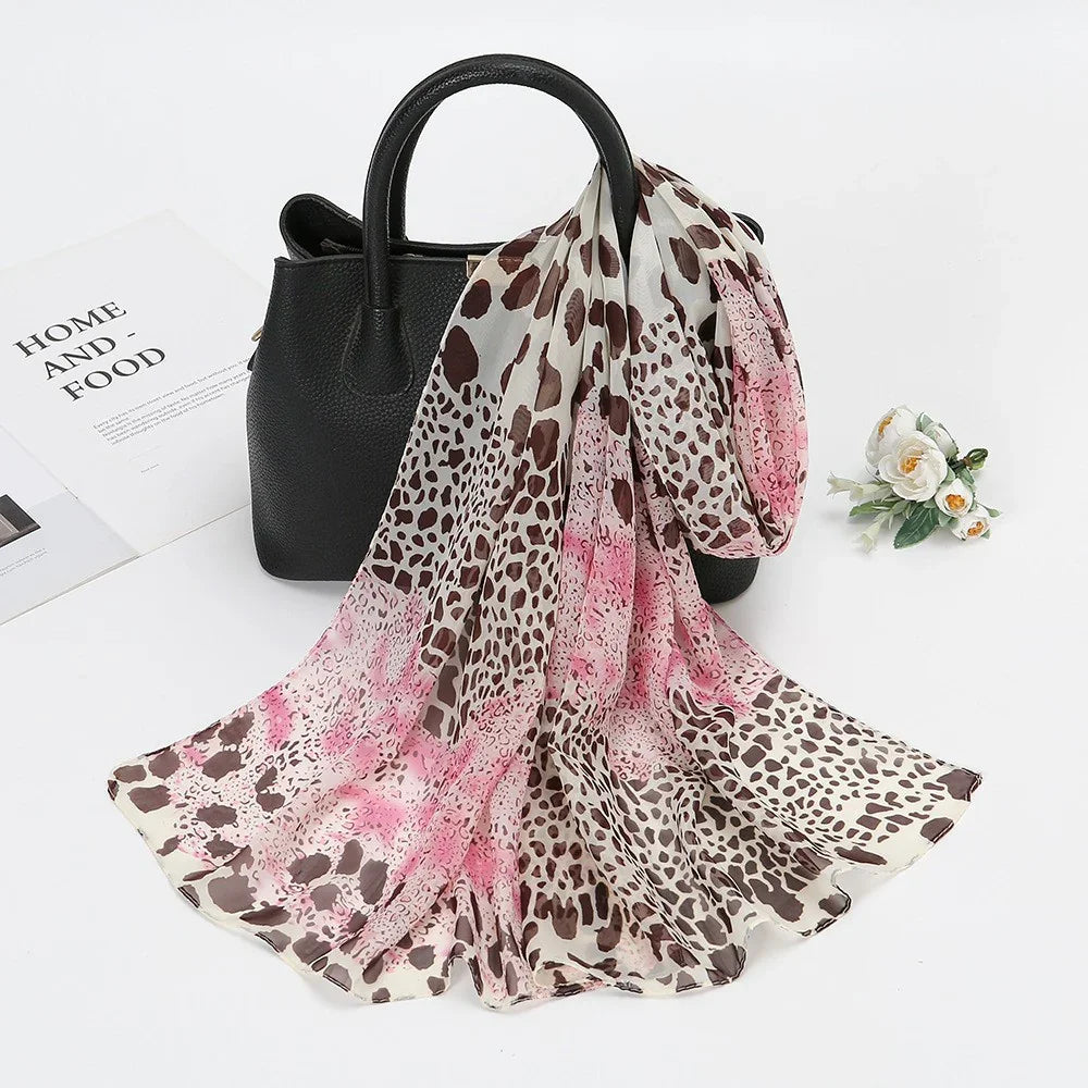 Leopard print scarf with pink accents draped over a black leather handbag on white surface