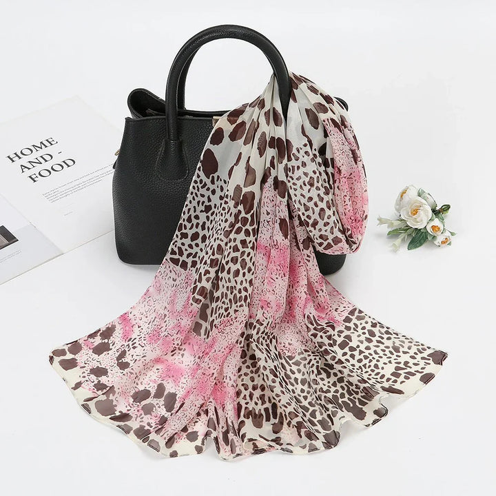 Leopard print scarf with pink accents draped over a black leather handbag on white surface